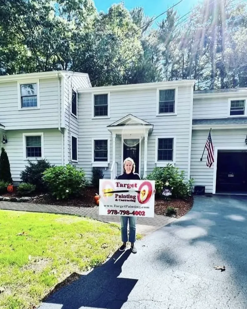 Homeowner holding a Target Painting yard sign in front of her freshly painted white colonial