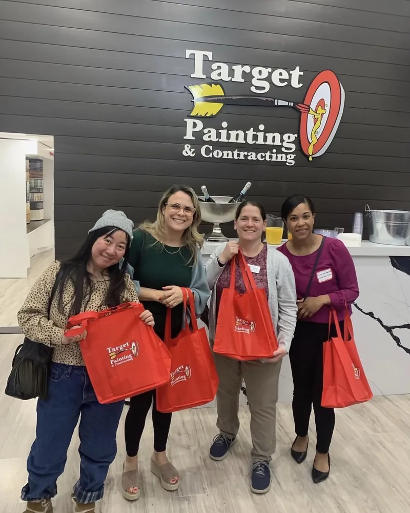 Four smiling guests holding red Target Painting bags under the logo at the Target Painting office